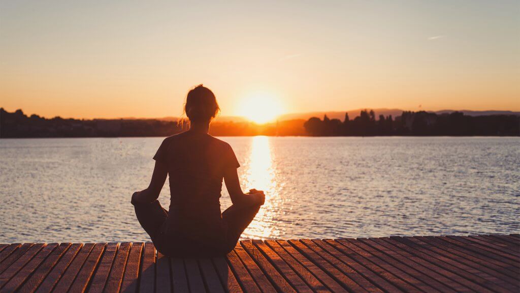 Woman meditating on a pier at sunset