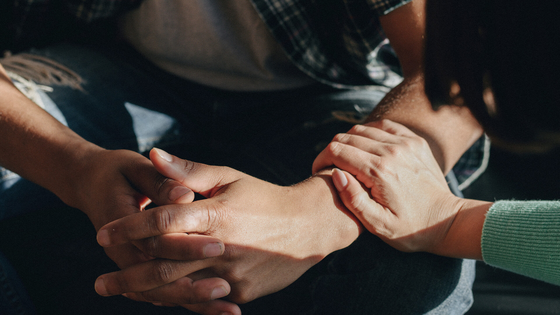 Closeup of a someone fingerlocking their hands, and a mental health first aider comforting them