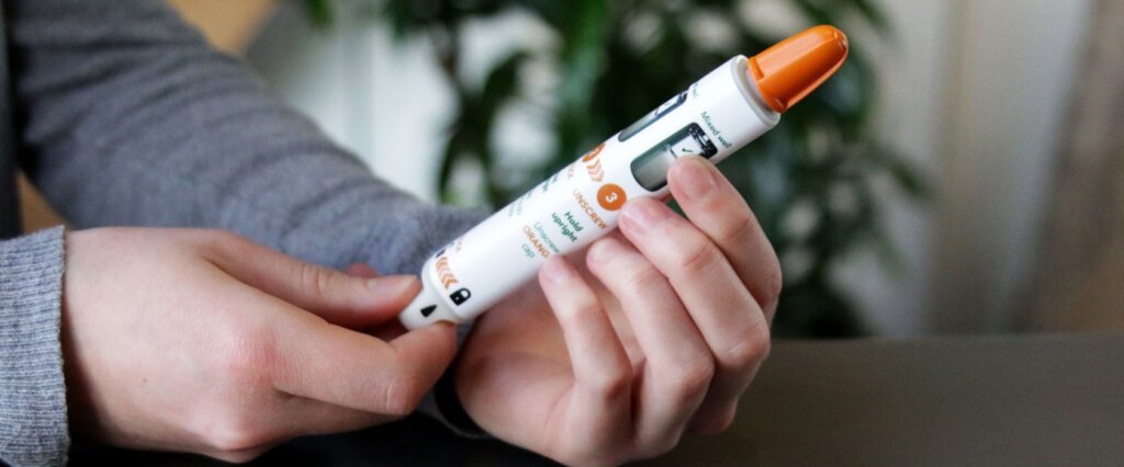 Hands Holding Trainer Auto Injector Pen  1024x426