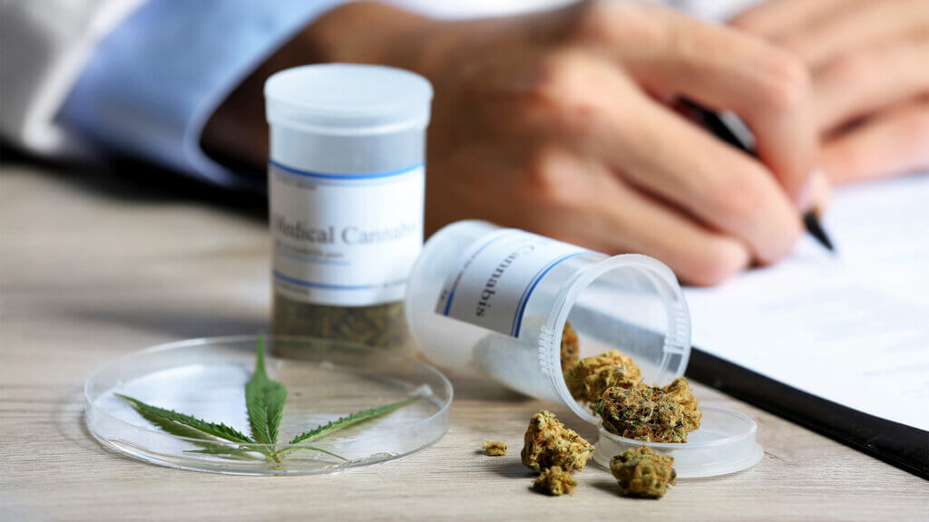 Doctor writing on prescription blank and bottle with medical cannabis on table close up