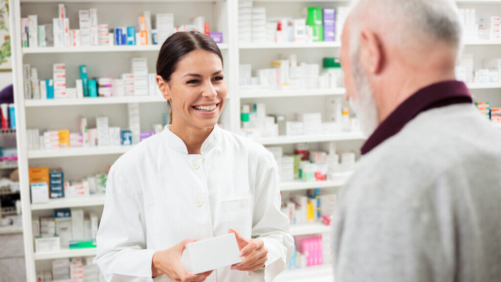 Happy female pharmacist giving medications to senior male customer