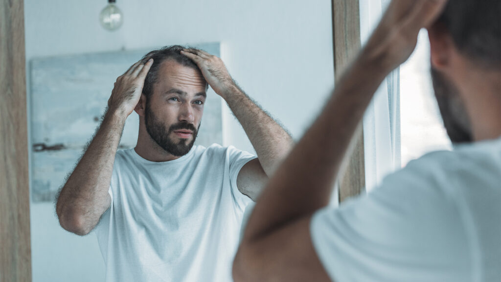 cropped shot of middle aged man with alopecia looking at mirror