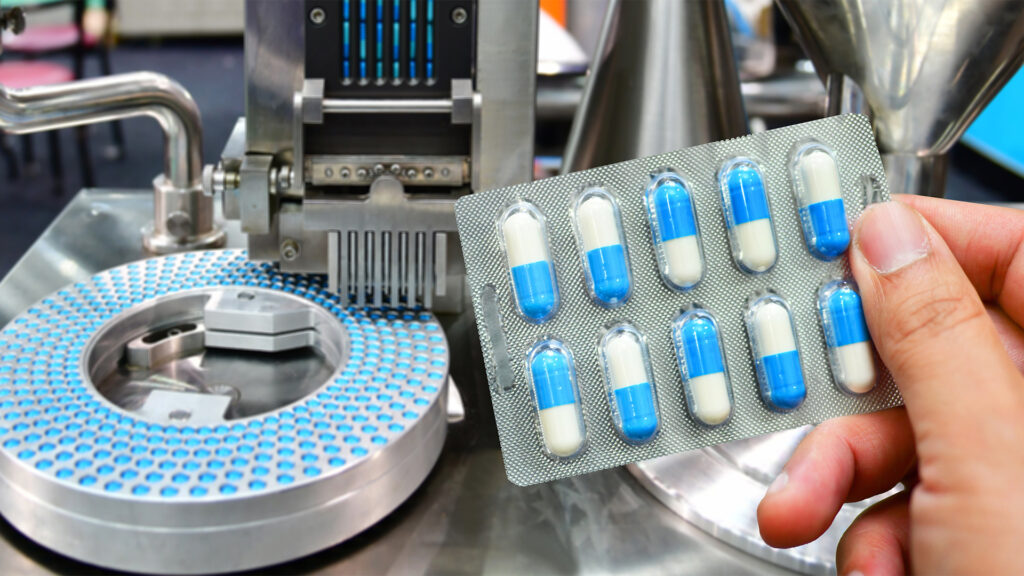 Hand holding blue capsule pack at medicine pill production line